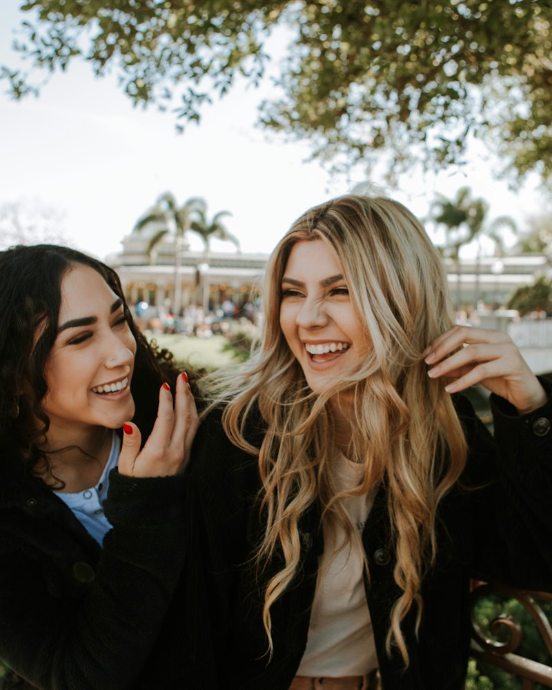 Zwei Frauen lachen gemeinsam unter Bäumen